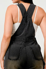 Person wearing black denim overalls over a white tank top against a plain background