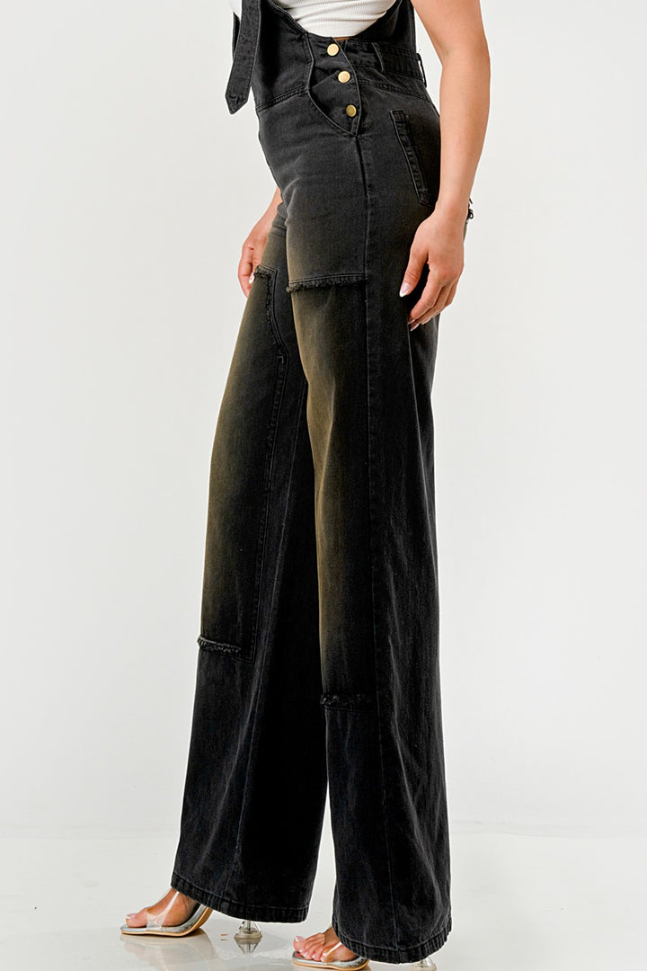 Person wearing black wide-leg overalls with a white background