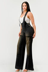 Woman wearing black overalls with a white top on a plain background
