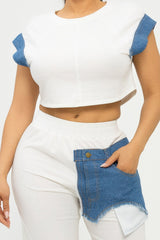 Person wearing a white top with blue accents and denim shorts on a plain background