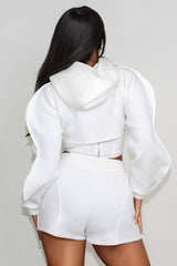 back view of woman wearing a white hoodie and shorts set against a plain background