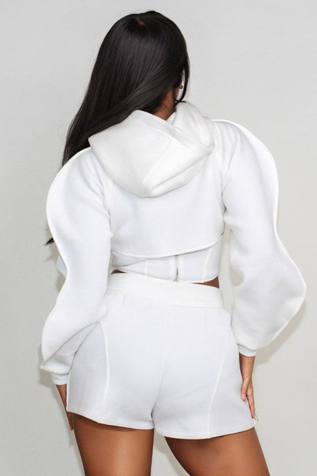 back view of woman wearing a white hoodie and shorts set against a plain background