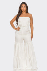 Woman wearing a white strapless jumpsuit on a plain background